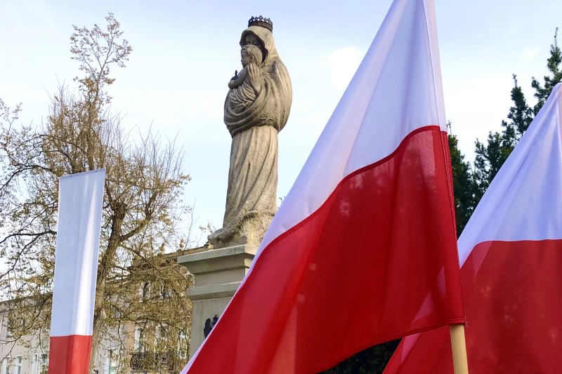 na zdjęciu widnieje flaga Polski oraz pomnik Matki Boskiej 