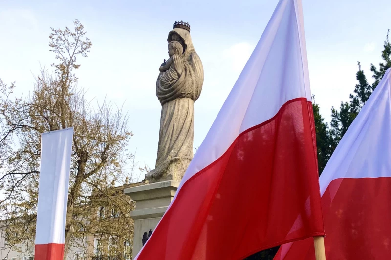 Na zdjęciu powiewające flagi Polski, w tle pomnik Matki Boskiej